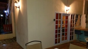 An outdoor dining area with a table and chairs, a sliding glass door, and wall-mounted lights.