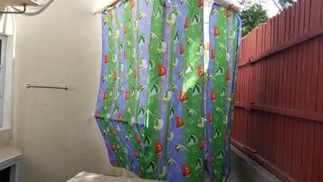 A bathroom with a shower curtain featuring a fish pattern, a window, and a red fence.