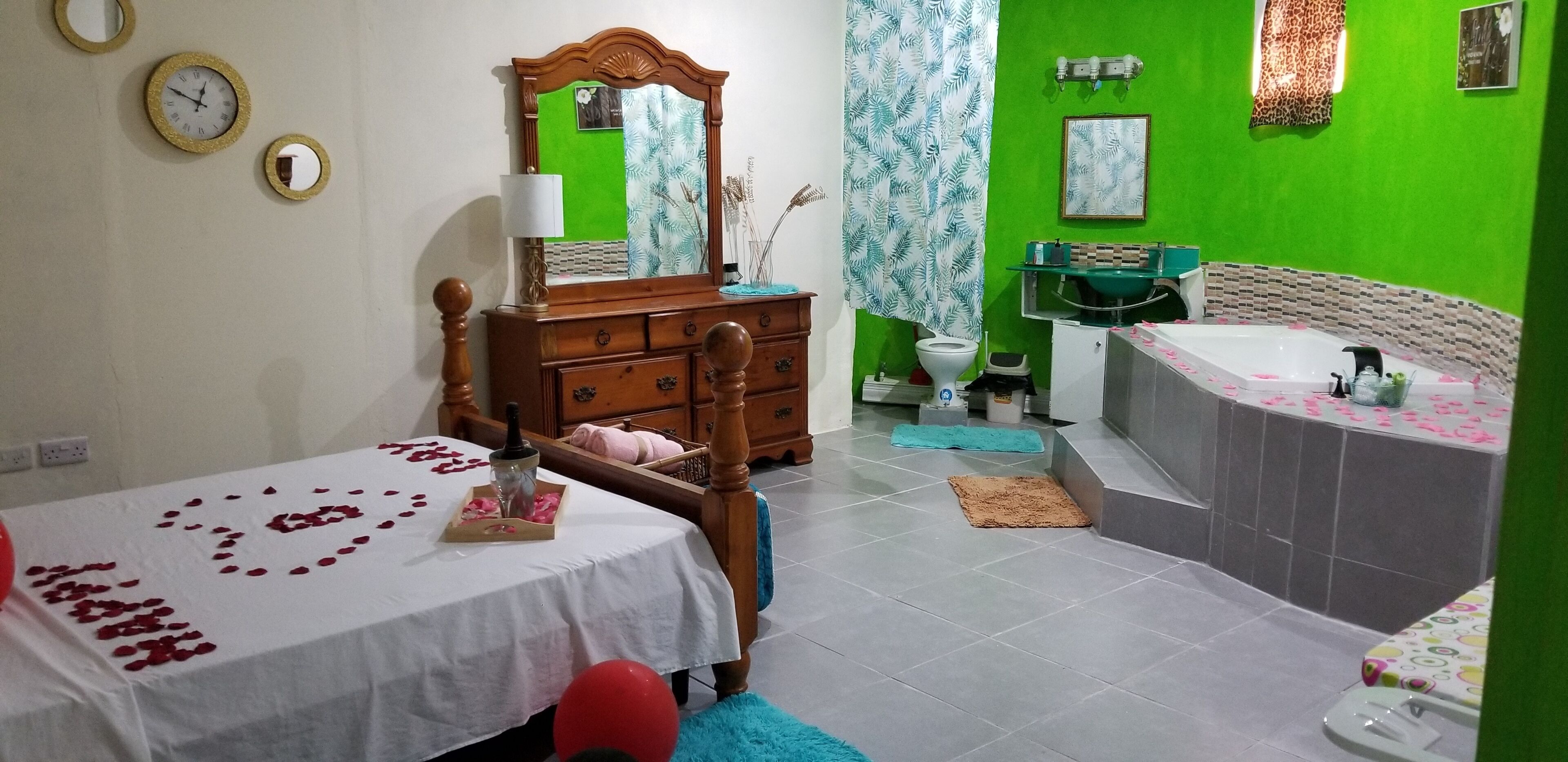A bedroom with a bed, dresser, vanity, and a bathtub.