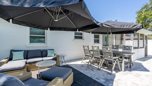 A patio with wicker furniture, a table, and chairs under large umbrellas. - Walk to the beach! Clean and new, remodeled  cozy 3 bedroom 2 bath cottage house (Venice)