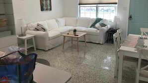 A living room with a white sofa, a coffee table, a lamp, and a window with a view of parked cars. - Walk to the beach! Clean and new, remodeled  cozy 3 bedroom 2 bath cottage house (Venice)