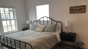 A bedroom with a metal bed frame, two bedside tables with lamps, a small trash bin, and a window with blinds. - Walk to the beach! Clean and new, remodeled  cozy 3 bedroom 2 bath cottage house (Venice)