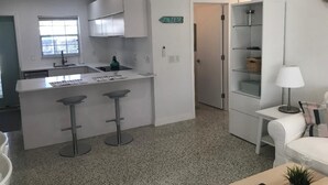 A modern kitchen with white cabinets, a bar area with stools, a countertop with a kettle, and a door marked "BEACH". - Walk to the beach! Clean and new, remodeled  cozy 3 bedroom 2 bath cottage house (Venice)