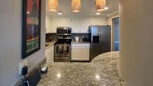 Una cocina moderna con armarios blancos, electrodomésticos de acero inoxidable, encimeras de granito e iluminación colgante.