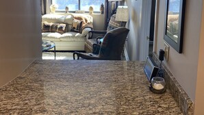 Una cocina moderna con encimeras de granito, iluminación colgante y vistas a una sala de estar acogedora con un sofá y sillones.