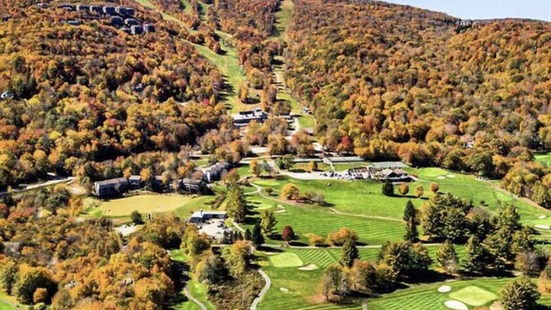 Un campo de golf con varios greens, un club de campo y zonas boscosas circundantes.