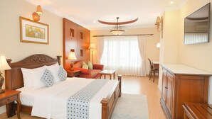 Ein Hotelzimmer mit Bett, Nachttischen, Schreibtisch, Stuhl, Kleiderschrank, Spiegel und einem fenster mit Vorhängen.