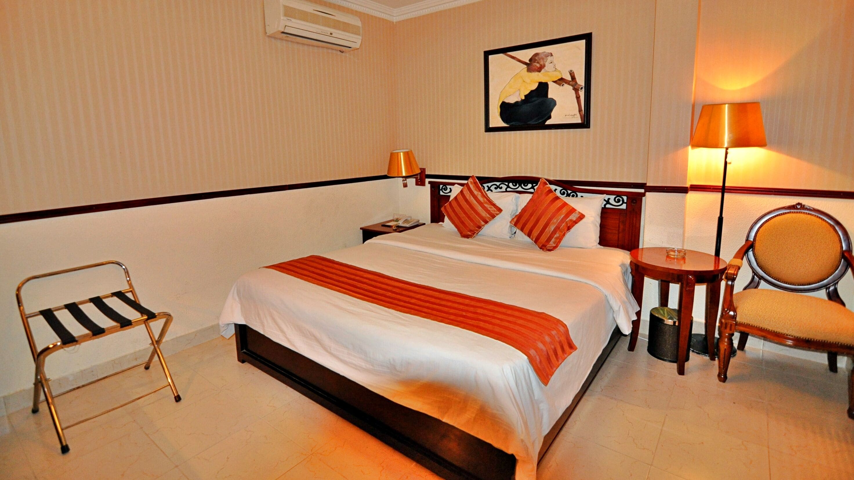 A hotel room with a bed, a chair, a nightstand, a lamp, and a picture on the wall.