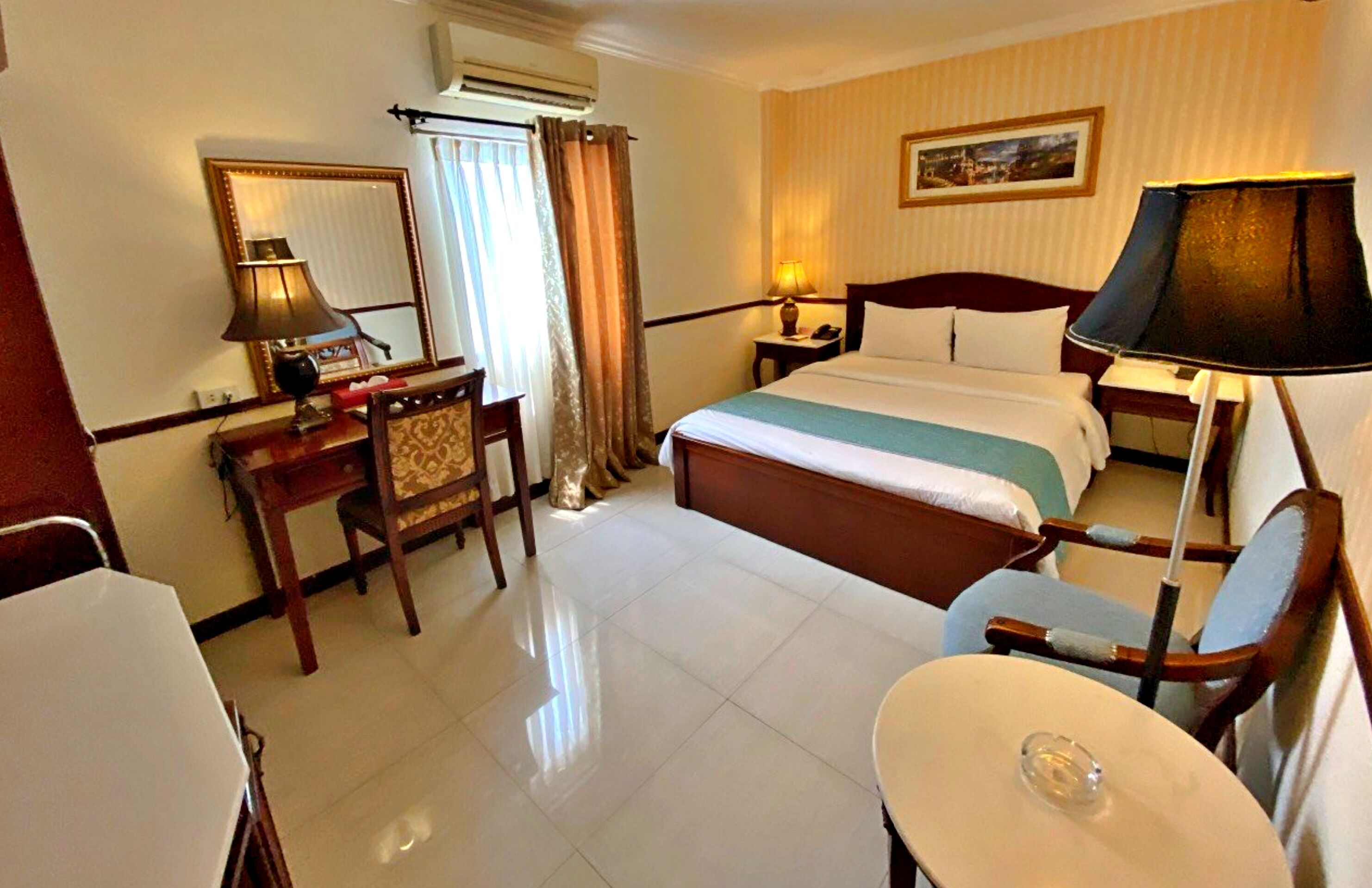 Una habitación de hotel con cama, mesita de noche, lámpara, silla, escritorio y una pequeña mesa.