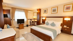 Ein Hotelzimmer mit einem Bett, Nachttischen, einem Schreibtisch mit Stuhl, einem Fernseher und einem großen Fenster mit Vorhängen.