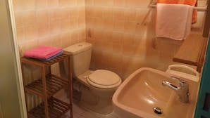 A bathroom with a toilet, sink, and a shelf with towels. - Les Océanides Villa 2 with sea view (Le Diamant)