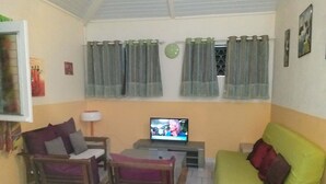 A living room with a green sofa, wooden chairs, a television, and curtains. - Les Océanides Villa 2 with sea view (Le Diamant)