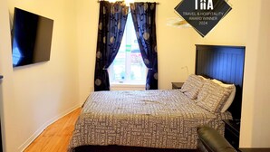 Un dormitorio con cama, televisor, ventana con cortinas e iluminación en el techo.