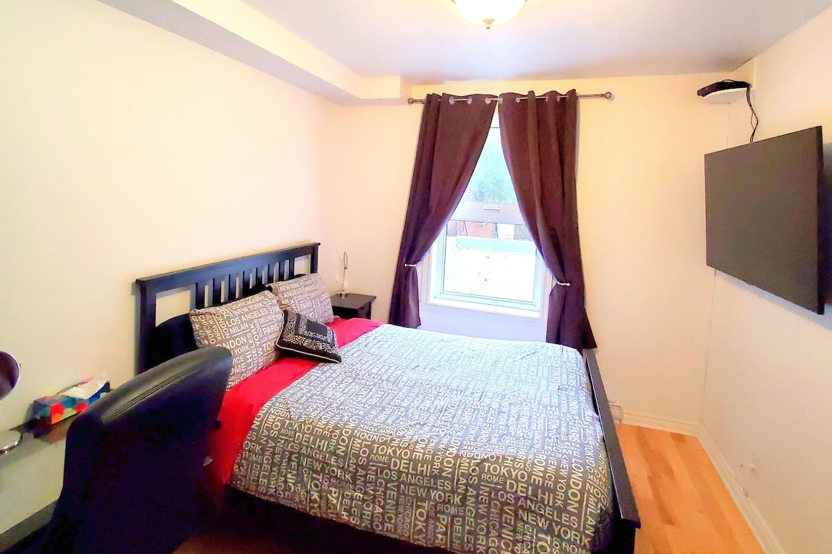 Un dormitorio con cama, escritorio, silla, televisión y ventana con cortinas.