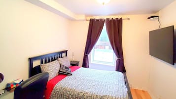 Un dormitorio con cama, escritorio, silla, televisión y ventana con cortinas.
