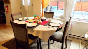 Un comedor con una mesa dispuesta para cuatro personas, sillas, un extintor y una ventana con cortinas.
