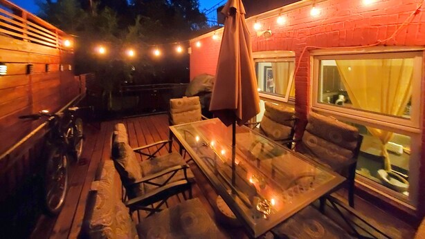 Un patio exterior con una mesa, sillas, una bicicleta y luces colgantes.