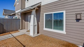 A two-story house with a covered patio area, a window with blinds, and a small outdoor utility box. - 3BR w fireplace, gaming TVs, mountain views! (Bellemont)