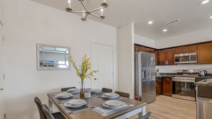 A modern kitchen with stainless steel appliances, wooden cabinets, and a dining area with a table set for four. - 3BR w fireplace, gaming TVs, mountain views! (Bellemont)