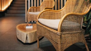 Una cadira de vimet amb coixí, una taula de fusta rodona i un panell de bambú vertical en un ambient interior modern.