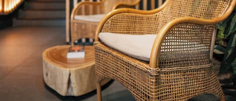 A wicker chair with a cushion, a round wooden table, and a vertical bamboo panel in a modern interior setting.