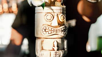 A tiki cocktail with a carved face, a straw, and a flower on a glass.