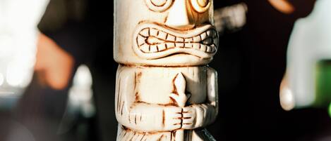 A tiki cocktail with a carved face, a straw, and a flower on a glass.