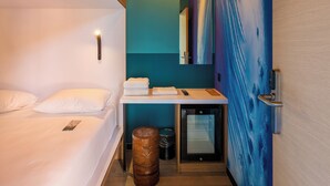 Habitació d'hotel moderna amb un llit, una petita taula de treball, un mirall i una paret amb un quadre de ones.