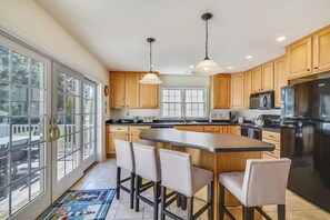 Una cocina amplia con armarios de madera, una isla grande con taburetes de bar y un refrigerador de acero inoxidable.