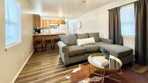 Uma sala de estar com um sofá modular cinza, uma mesa de centro de vidro e um ventilador de teto.