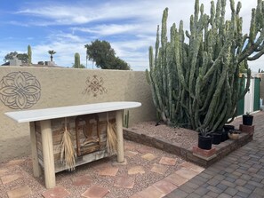 Um jardim de cactos com um banco de madeira e arte decorativa na parede.
