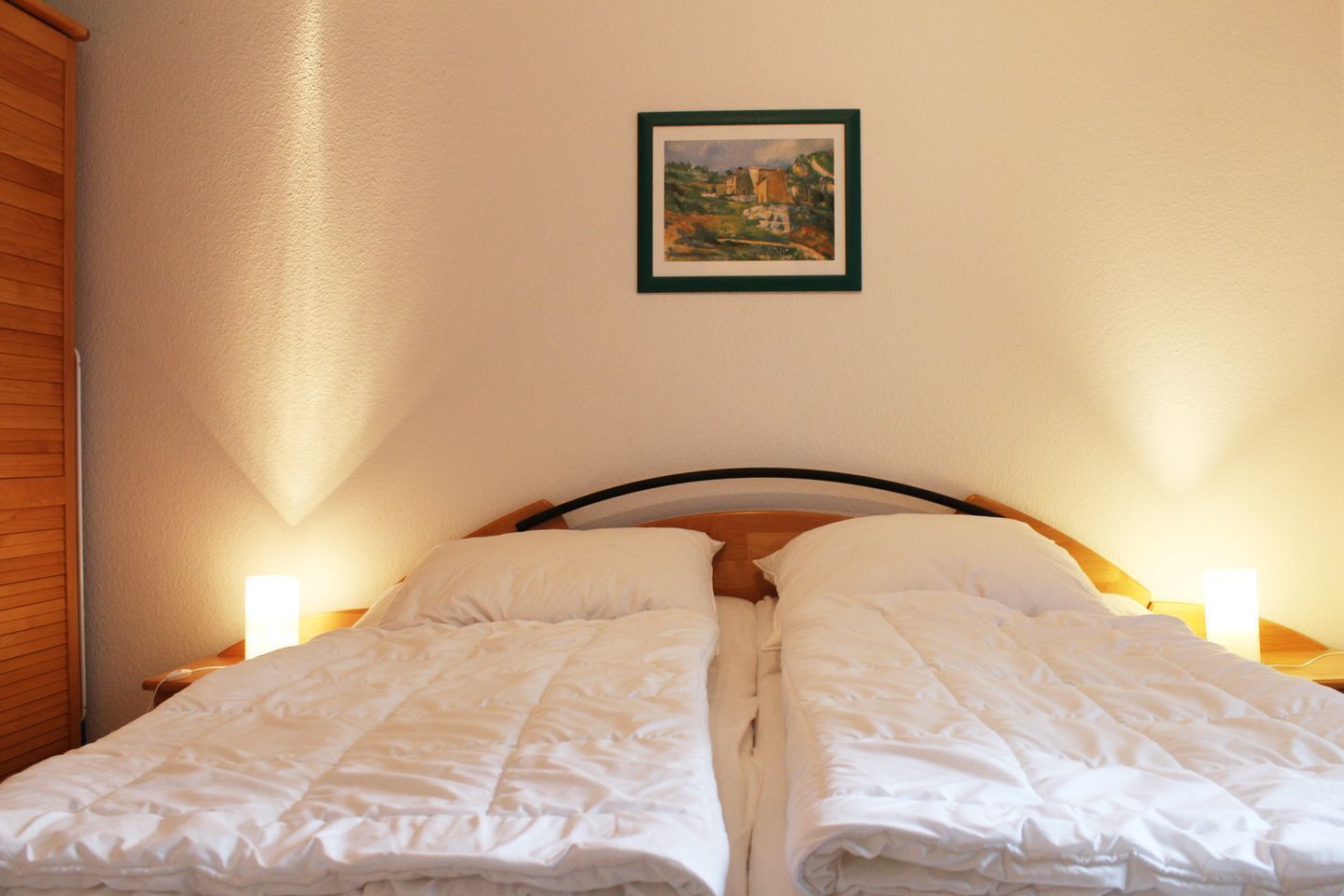 Ein Doppelbett mit weißer Bettwäsche, zwei Nachttische mit Lampen und ein gerahmtes Bild an der Wand.