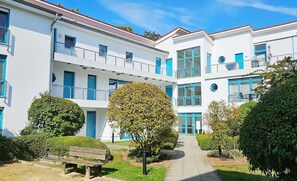 Um edifício moderno com várias varandas, um caminho central e áreas verdes bem cuidadas.