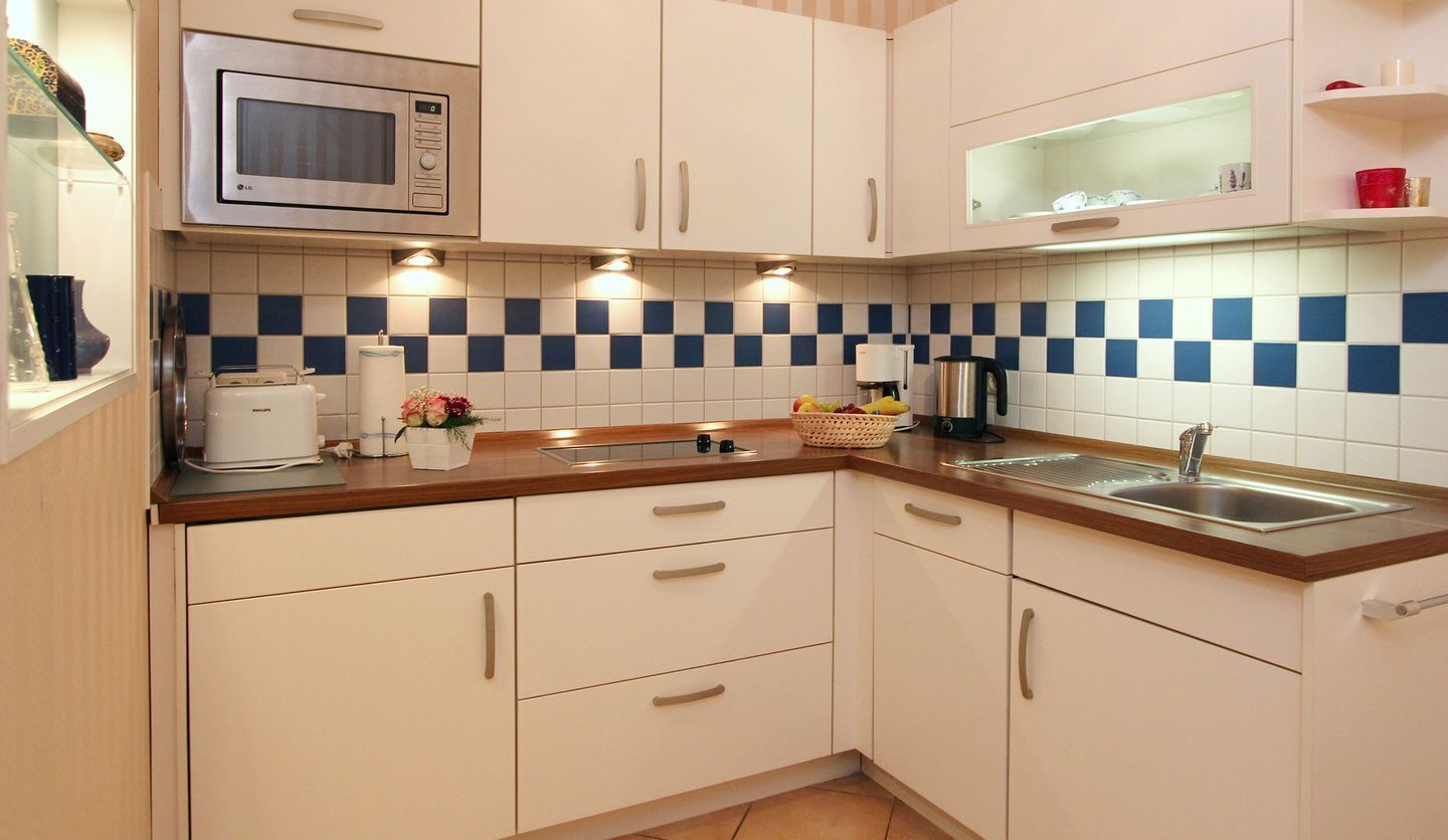 A kitchen with white cabinets, a microwave, a sink, and a checkered backsplash.