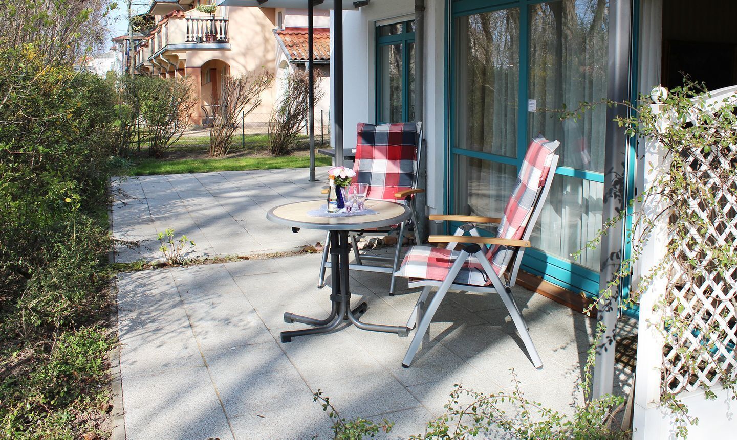 An outdoor seating area with a table and two chairs, a glass door, and a view of a residential building.