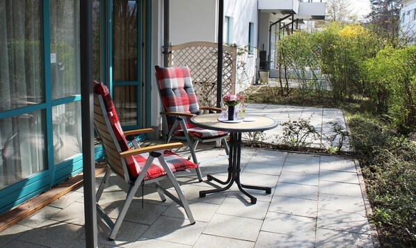 Une terrasse avec deux chaises et une table, une clôture en bois et un petit espace aménagé en jardin.