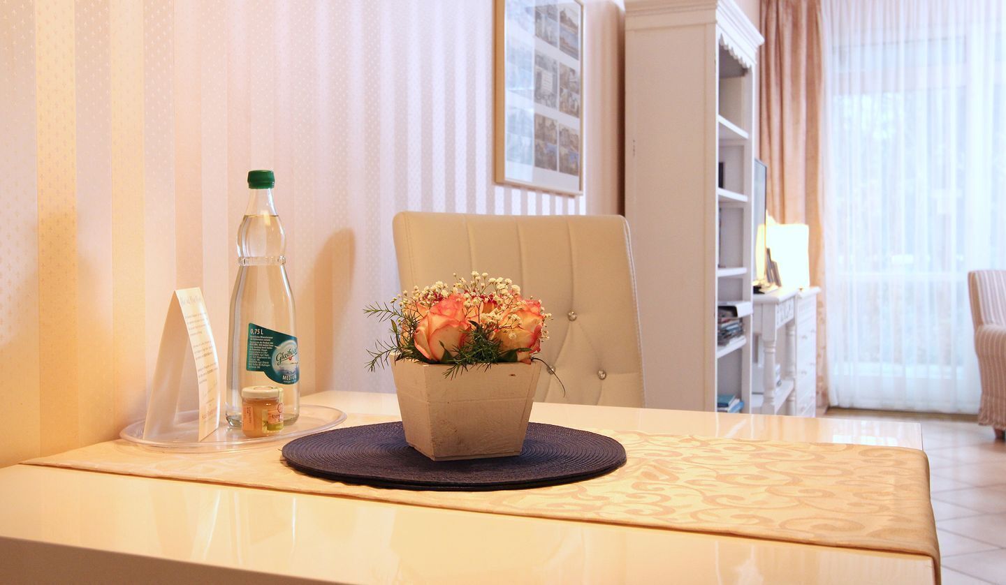 A hotel room with a dining table, a potted plant, a bottle, and a menu stand.