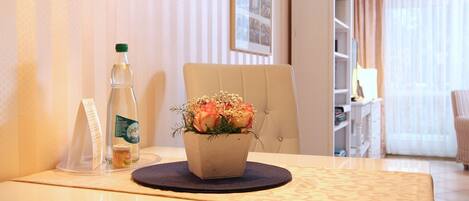 Een hotelkamer met een eettafel, een potplant, een fles en een menukaartstandaard.