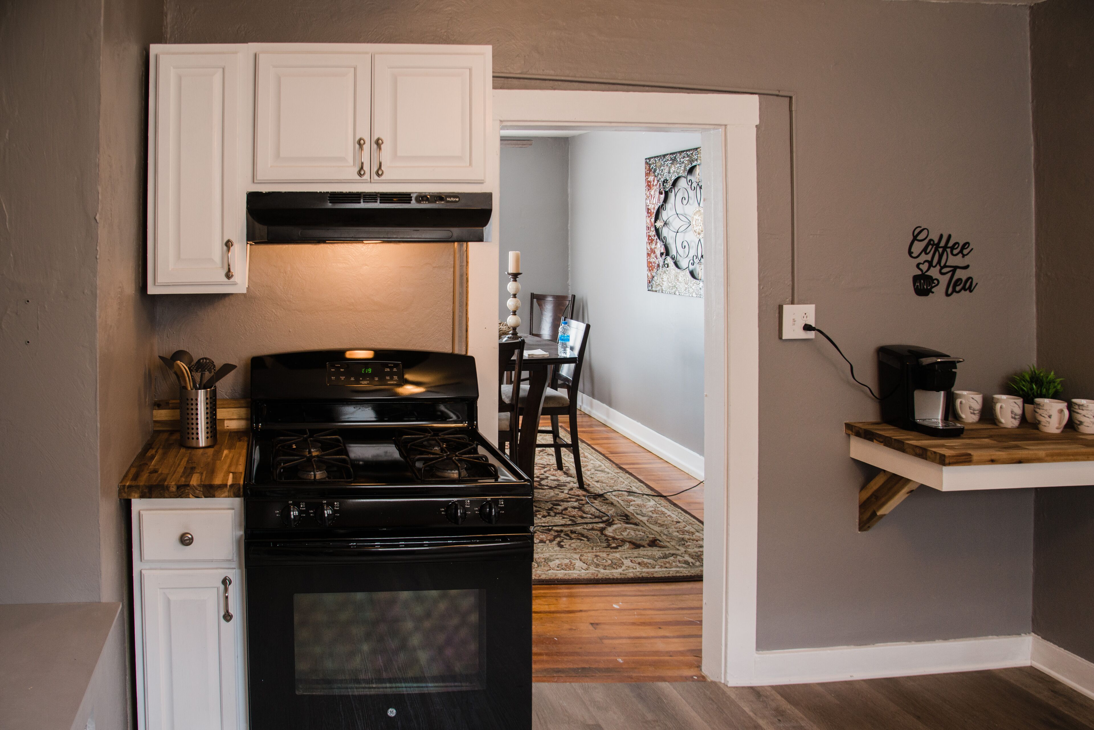 A kitchen with white cabinets, a black stove, and a coffee station.
