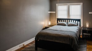 Un dormitorio con cama, mesitas de noche, ventilador de techo y ventana con persianas.