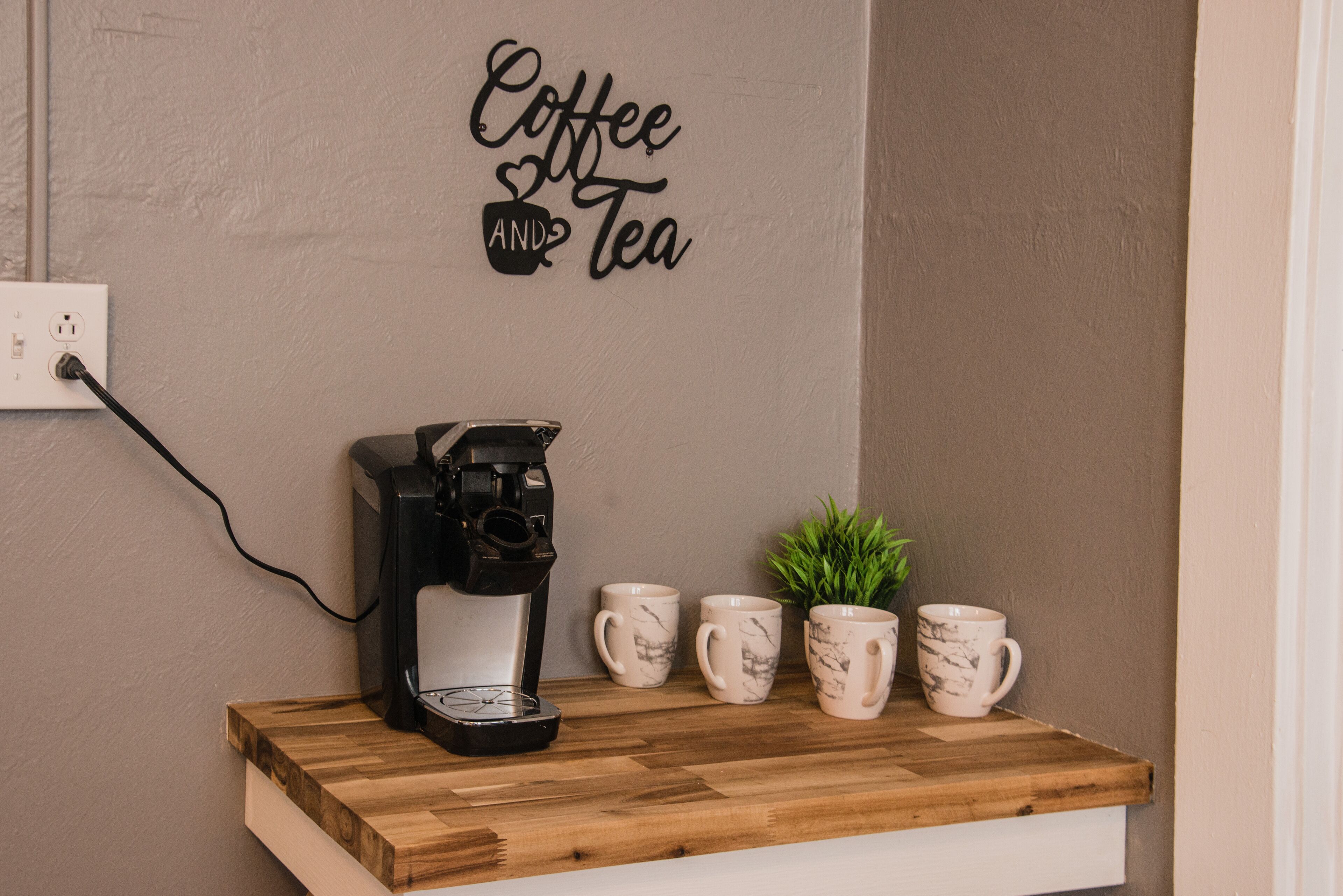 A coffee machine on a wooden shelf with four coffee cups and a small plant beside it.