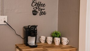 Una cafetera sobre un estante de madera, con cuatro tazas de café y una pequeña planta al lado.