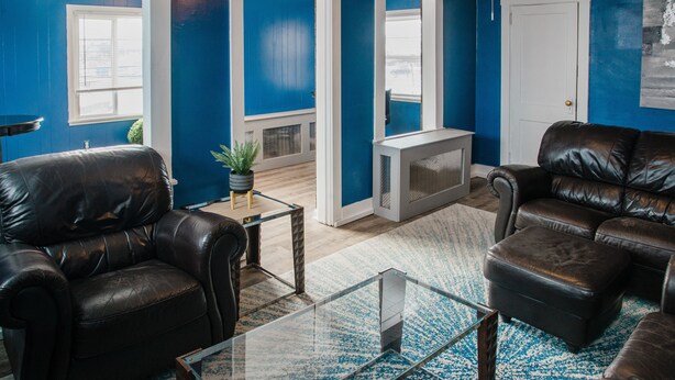 Una sala de estar con paredes azules, una mesa de centro de vidrio, sofás de cuero y una puerta blanca.