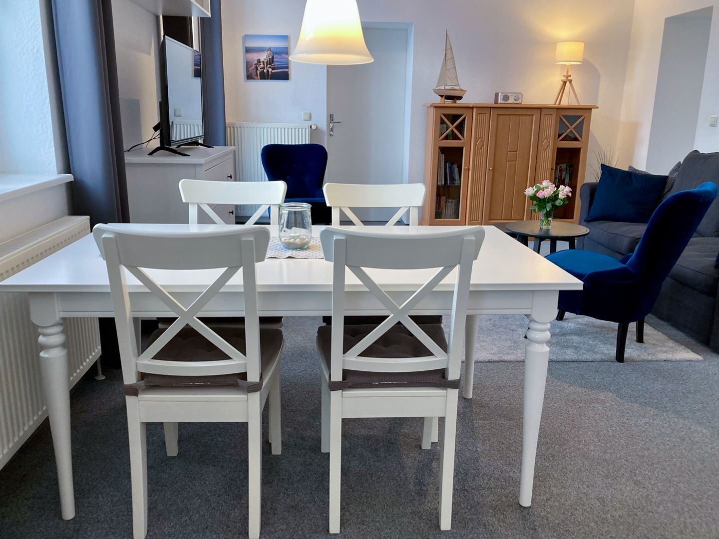 Una sala de estar moderna con una mesa de comedor, sillas blancas, un sofá azul y un mueble de madera con libros.