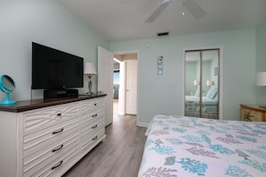 Quarto com cama, televisão sobre uma cômoda, espelho e porta para outro espaço.