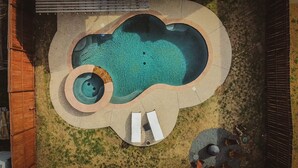 Un jacuzzi circulaire avec une petite piscine, entouré d’une zone sablonneuse où sont disposées des chaises longues.