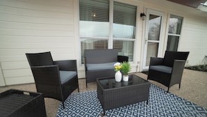 Une terrasse dotée de meubles en osier, d’une table basse en verre et de tapis d’extérieur à motifs.