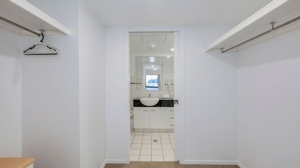 A narrow hallway leading to a bathroom with a sink, mirror, and hanging clothes rack.