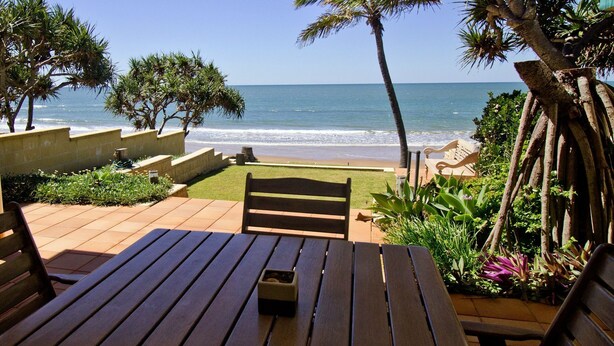 Una mesa y banco de madera en un patio con vista al océano.