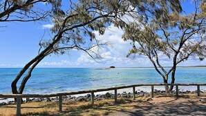 A coastal view with a clear sky, a sandy beach, and a wooden fence.